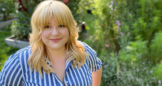 Student in blue and white stripe shirt with garden in background