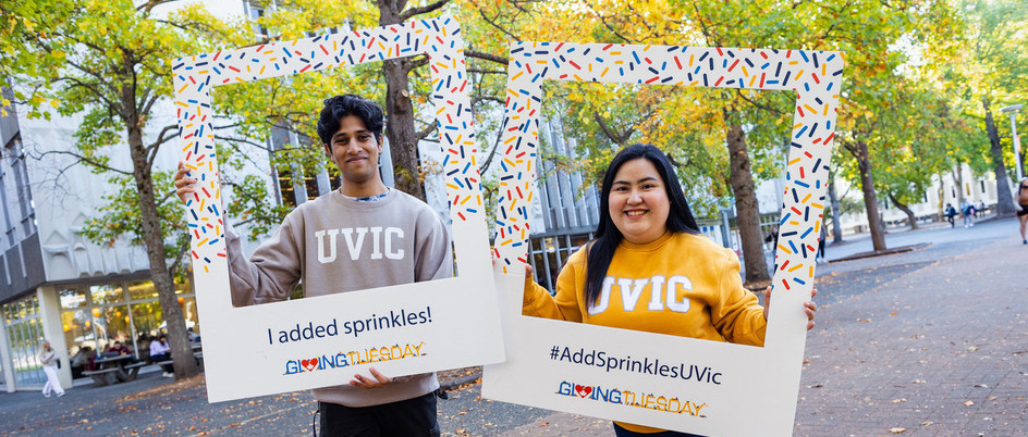 two students holding large instagram style frames that say "I added sprinkles" and "#UVicaddsprinkles"