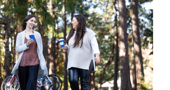 Two women walk talking to each other and holding blue Giving Tuesday coffees