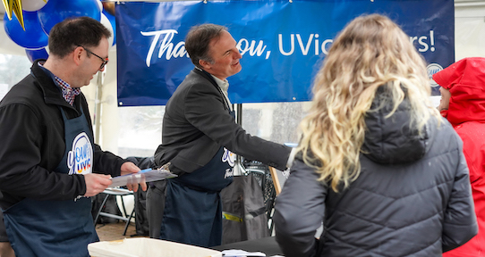 two men smiling wearing UVic aprons and handing women ice cream