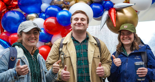 three students smiling in front of balloon arch