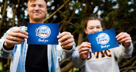 two students smiling and holding thank you cards
