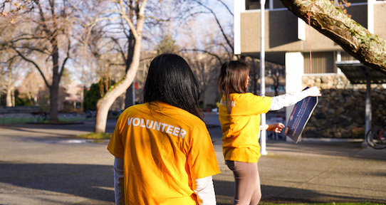 two women wearing yellow volunteer shirts hang tag in tree