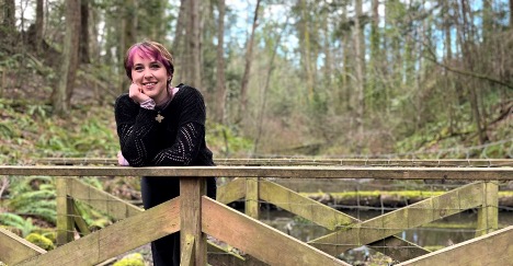 Jade stands on a bridge in the forest smiling at the camera