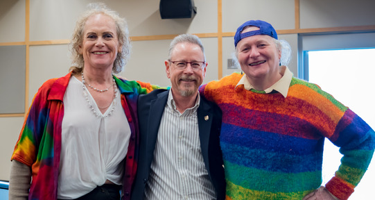 Dr. Aaron Devor stands smiling in the middle of two attendees at the Moving Trans History Forward conference.