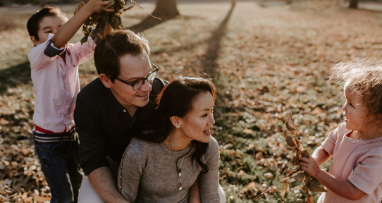 A man and woman sit on the grass smiling at two young children