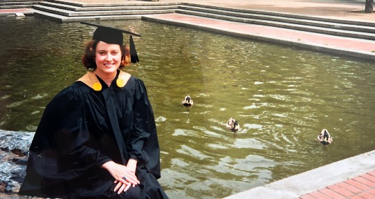 Patricia Collins sitting at the UVic fountain in her convocation regalia in 1997 