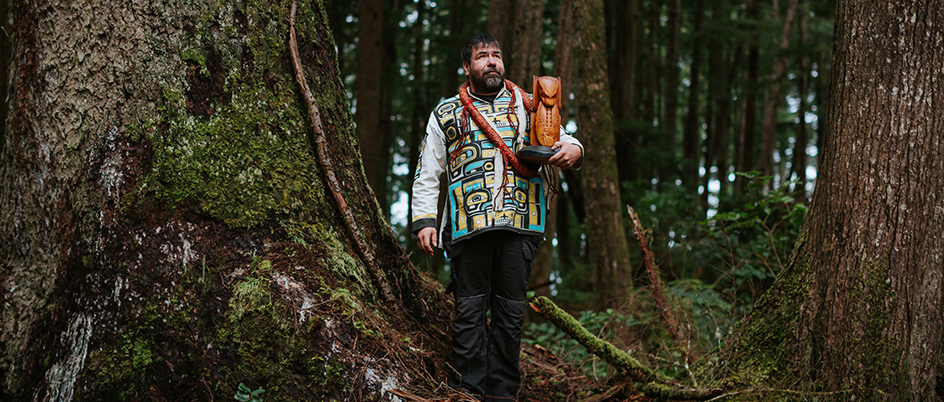 Chief Knox standing in a forest holding a carved object