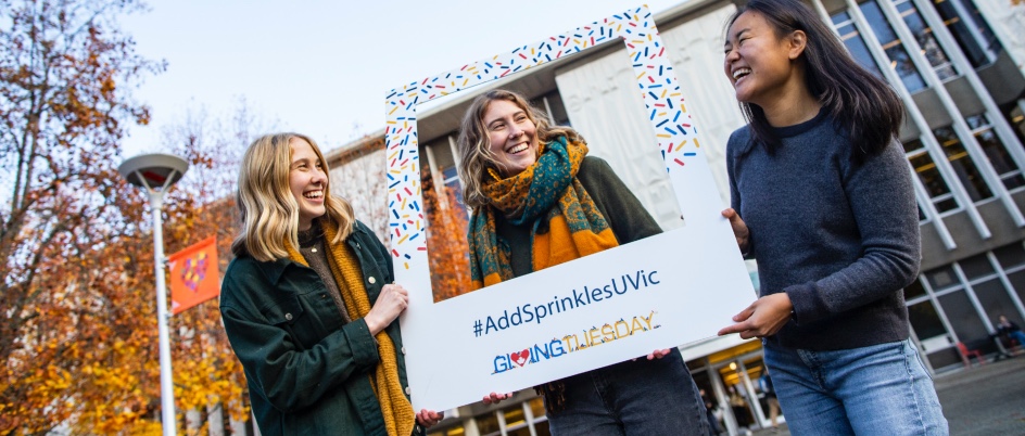 Three students hold a large instagram frame which has the hashtag Add sprinkles UVic