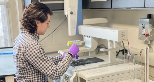 Researcher holding pipette standing next to specialized lab machinery. 