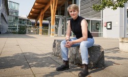 Student sitting on stone bench with university building in background