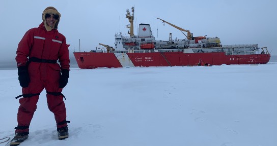 A person stands on a flat plain of ice in front of a coast guard vessel.