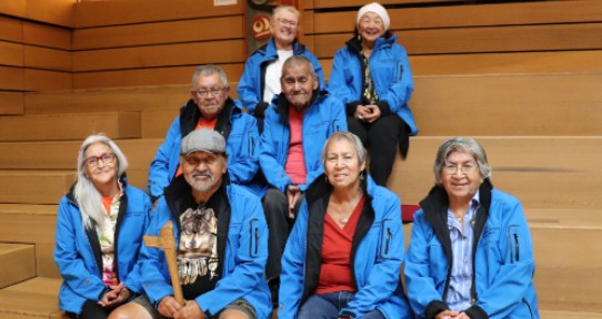 Eight Elders wearing blue jackets sitting on steps inside the university's First People's House