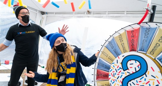 The president and a student look towards a colourful wheel spinning which has various words written on it