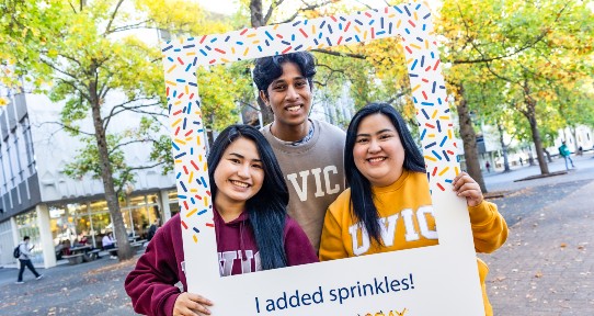 three students smiling holding a sprinkle frame
