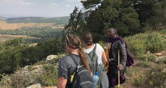 Three people with backs to camera looking out on a valley in Tanzania