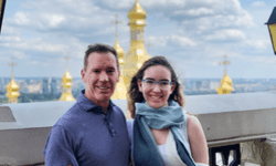 Dale and Sienna stand beside each other smiling at the camera. Behind them are large gold church-like structures