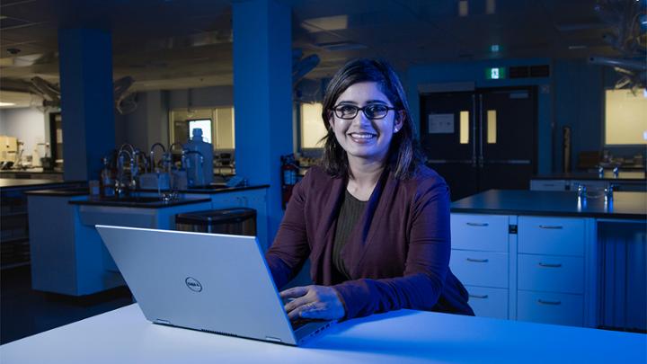 A female student of south asian descent working in a lab at a laptop