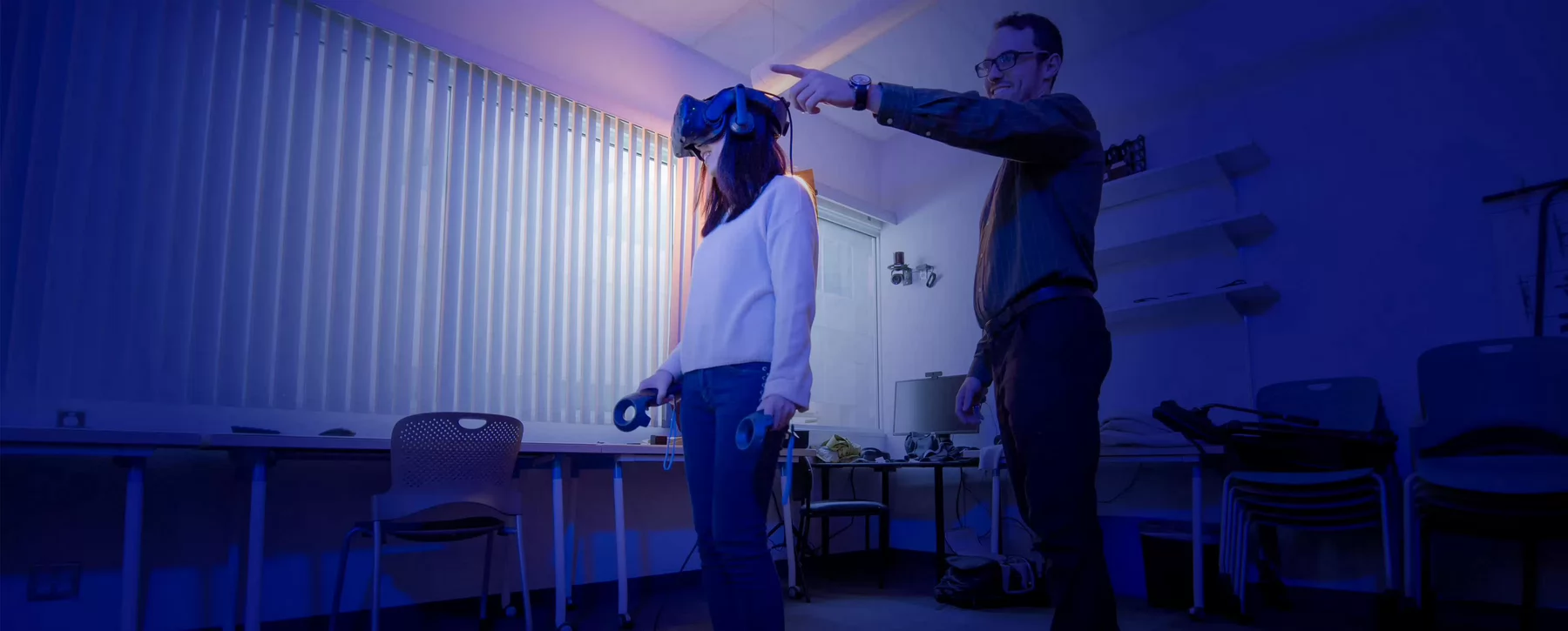 A grad student demonstrates a VR system while their supervisor directs them.