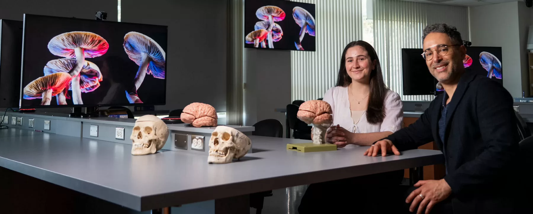 UVic researchers Baeleigh VanderZwaag and Mauricio Garcia-Barrera sit in a lab surrounded by images of psychedelic mushrooms.