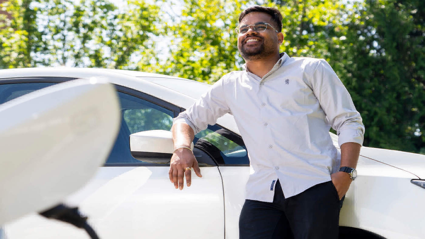 UVic Sustainability Scholar, Akash Mohanty, smiling and leaning against a UVic electric car.