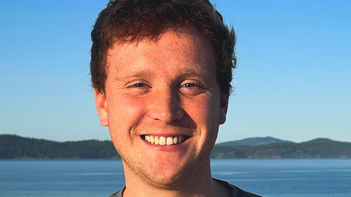 Sustainability Scholar, Liam Janke, pictured smiling with ocean and mountain background