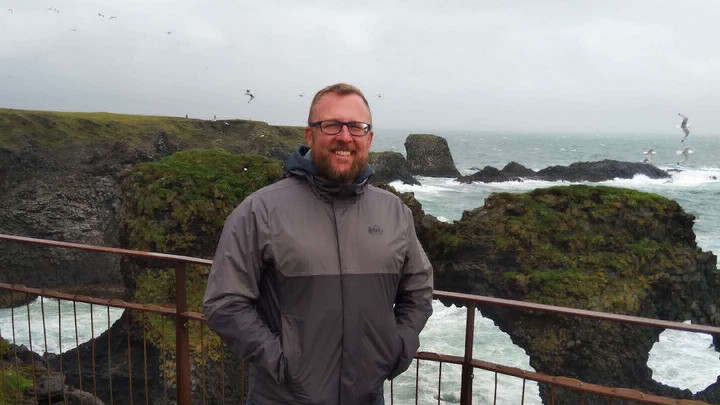 Student pictured smiling in front of ocean and cliffs