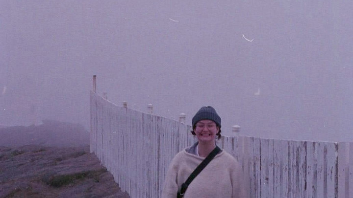 Sustainability Scholar Natasha Danais pictured in front of a white fence with misty hills and lighthouse in the background