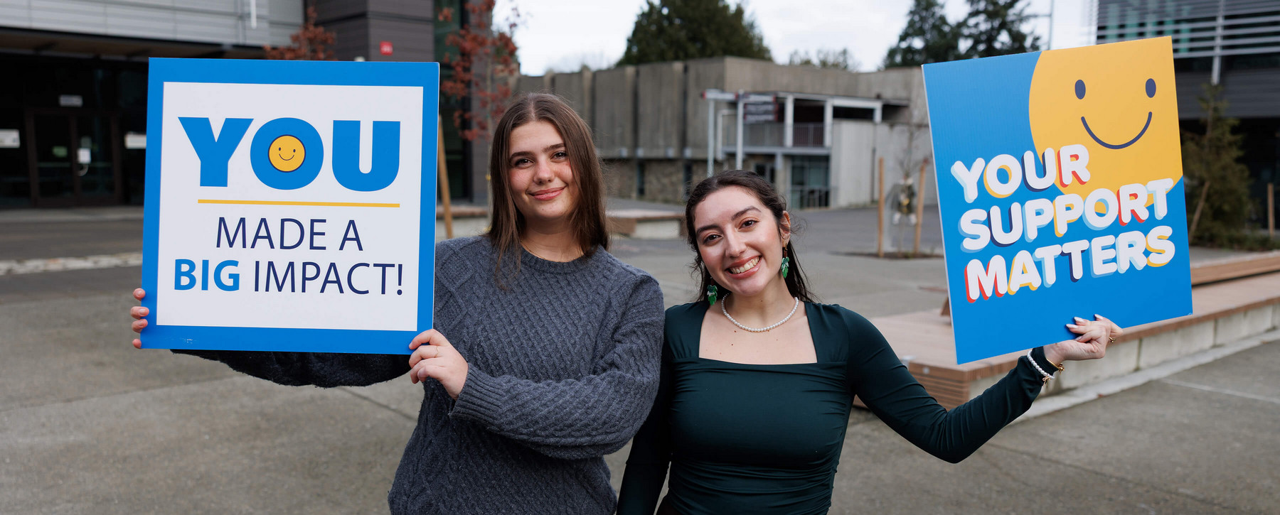 Two BCom students holding up thank you signs for donors
