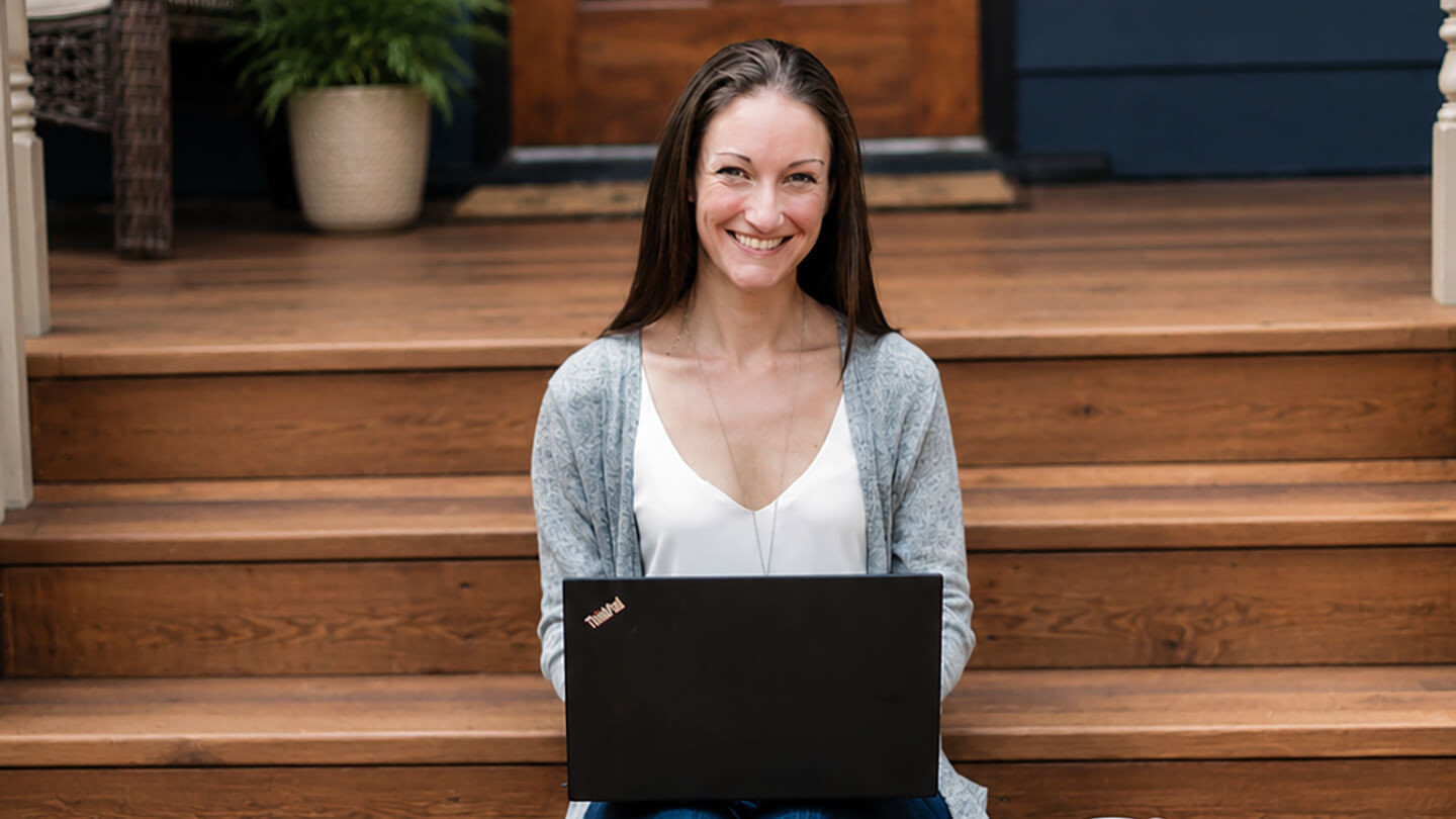 Jen Scharien sitting on the stairs to a house with a laptop