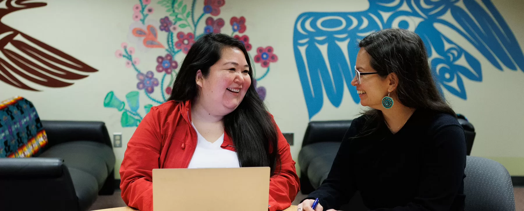 Two people at the Indigenous Student Support Centre smile at one another while sitting at a table.