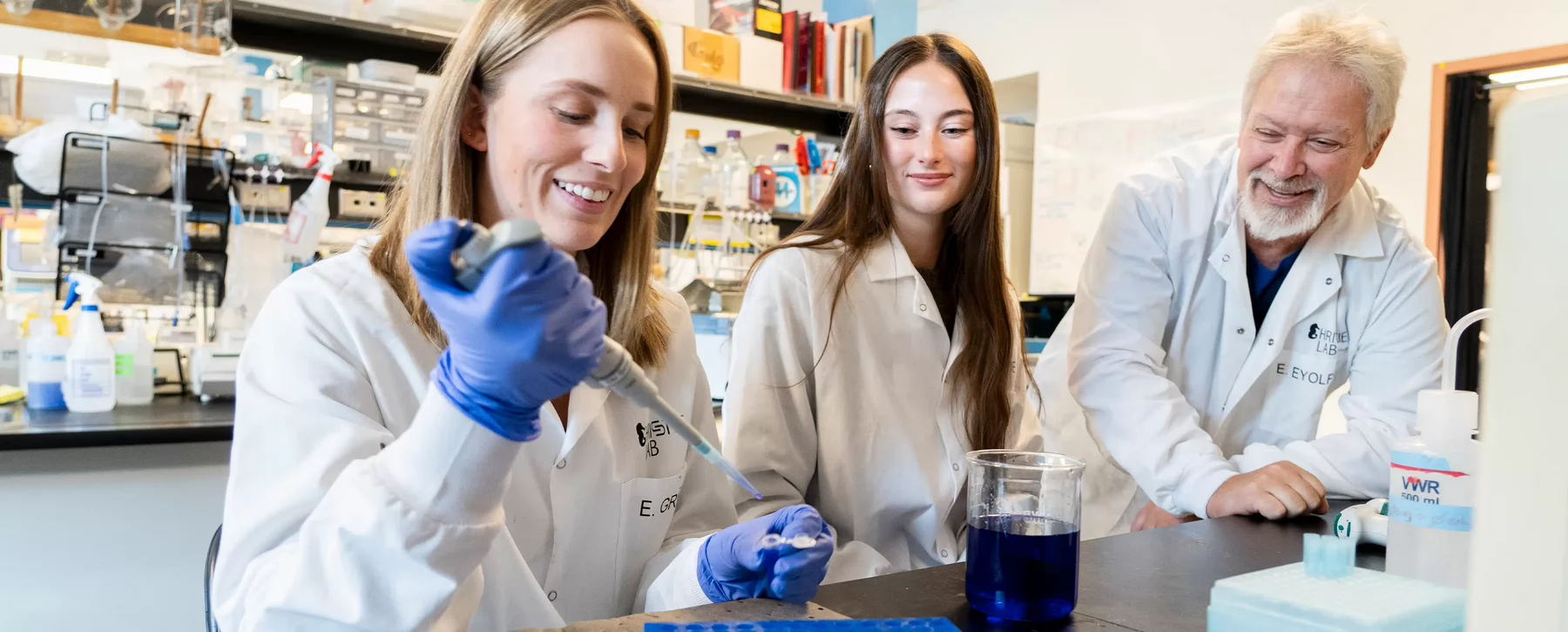 Three people in lab coats work on samples in a science lab.