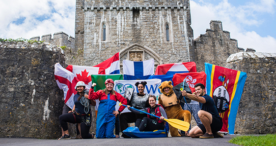 Co-op students holding their country flags in front of Atlantic College in Wales