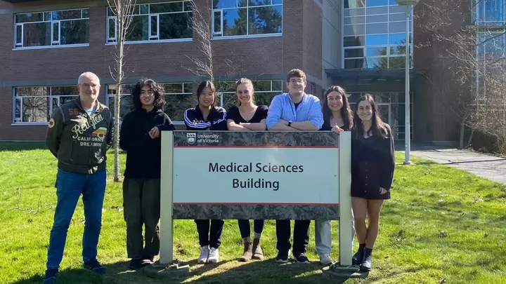 Group of students and Dr. Caruncho standing by a School of Medical Sciences sign