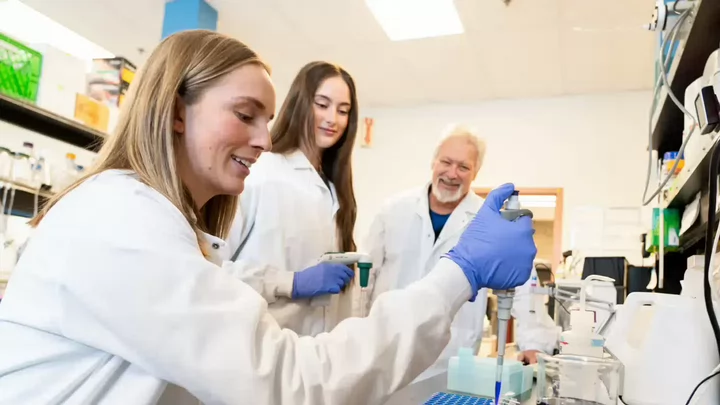 Woman in a lab coat conducts an experiment while two other researchers observe in background