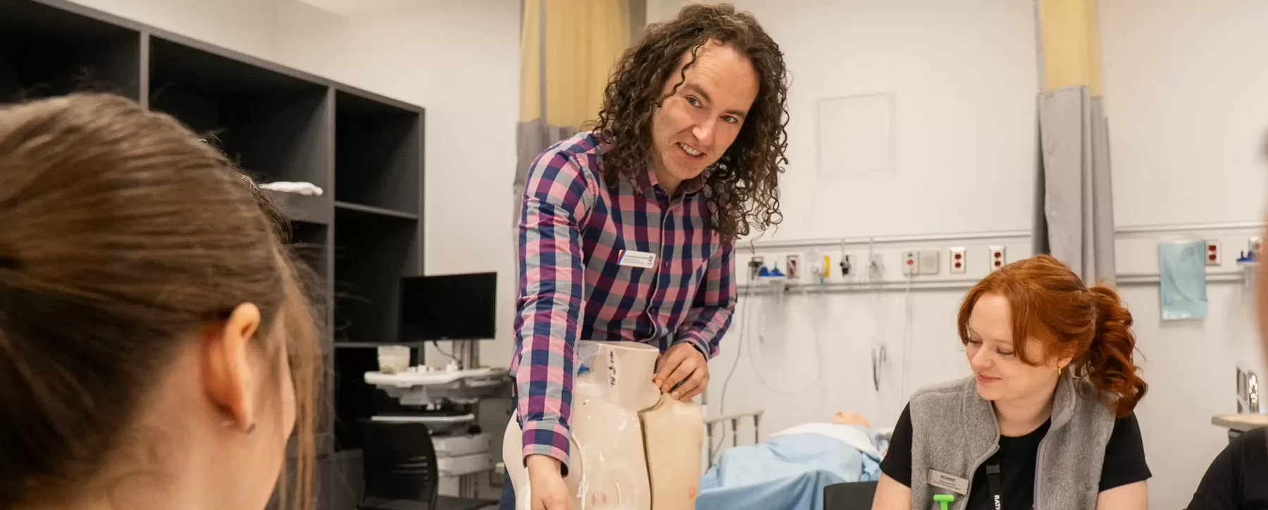 Man with long hair instructing students seated in foreground
