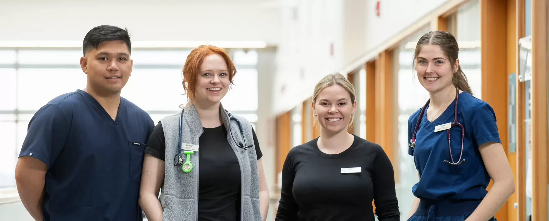 Four nursing students standing in a hallway and looking towards the camera