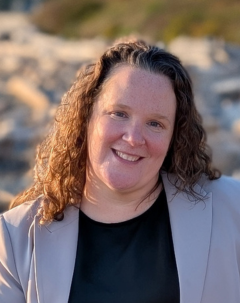 Portrait of Marcey Norman wearing a black blouse and grey blazer and a smile