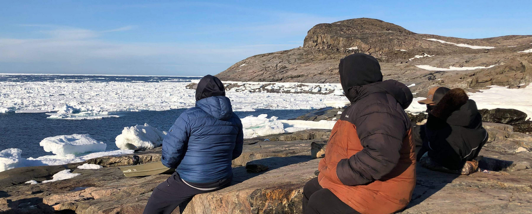 Three people in winter jackets looking over body of water covered in ice