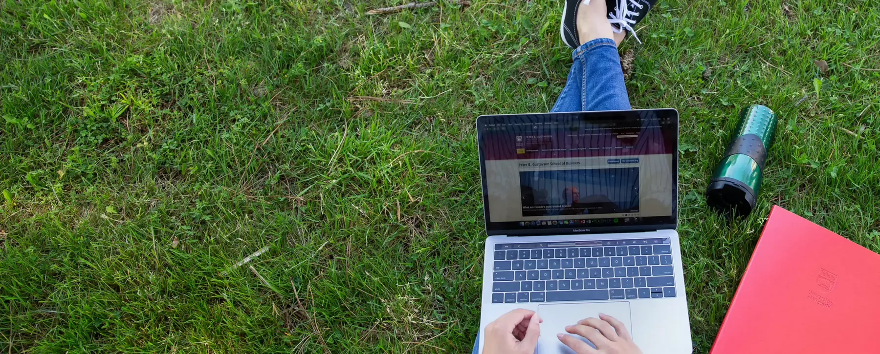 Overhead view of a student sitting on the grass with a laptop on their lap