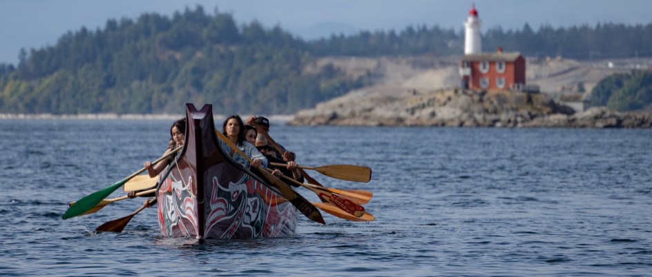 Students paddle a canoe to shore with a lighthouse in the background