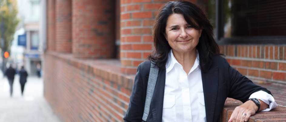 Nancy Clark, smiling, leans against a brick building in downtown Victoria