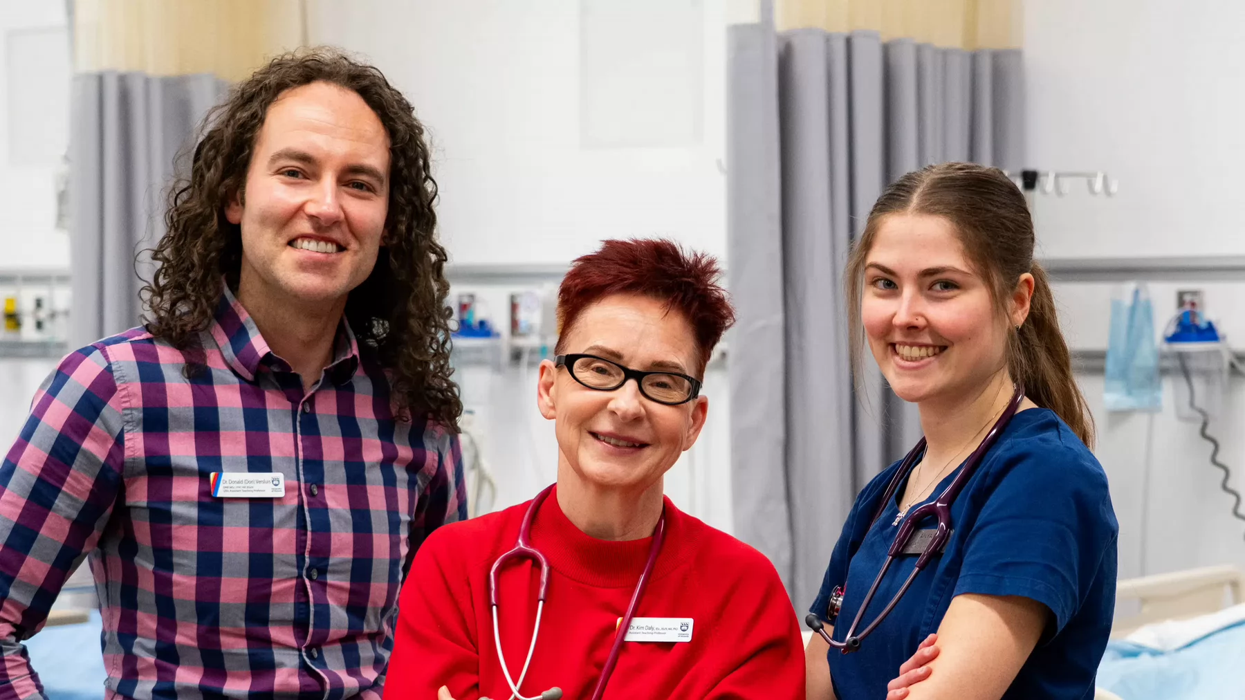 Three people standing and smiling in front of a hospital bed