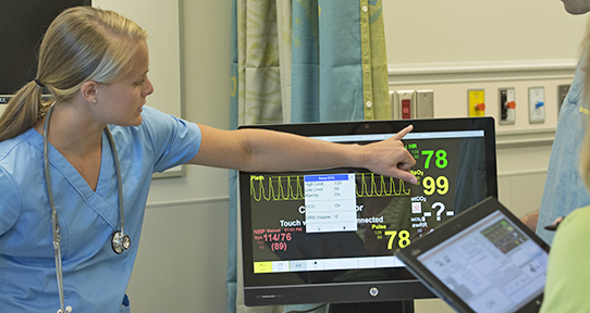 Nurse gesturing to a monitor showing vitals