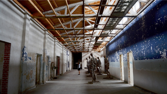 A shot of a long hallway featuring sculptures and museum exhibits, with one person looking thoughtfully.
