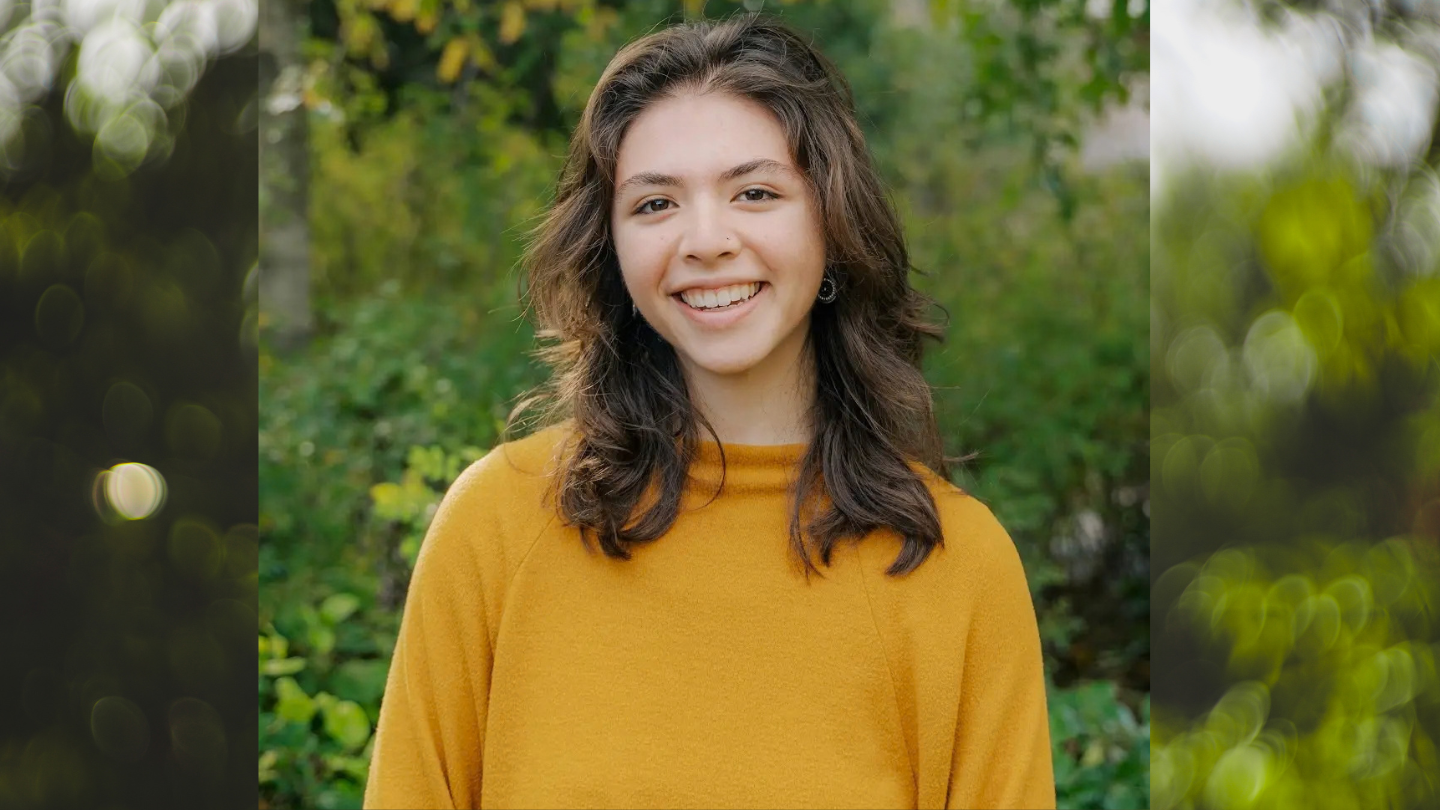 Ana Galicia wearing a yellow sweater in front of a blurry green background suggesting trees.