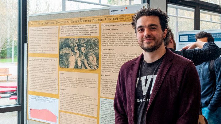 Braedon Lowey stands in front of a research poster, sharing his work at the JCURA research fair.