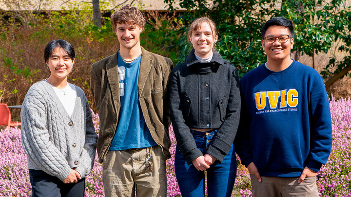 Four students from programs in the SLLC are standing outside in a row, smiling, on a bright spring day.