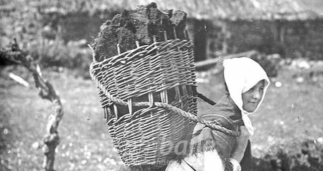 Woman carrying large basket of peat on her back.