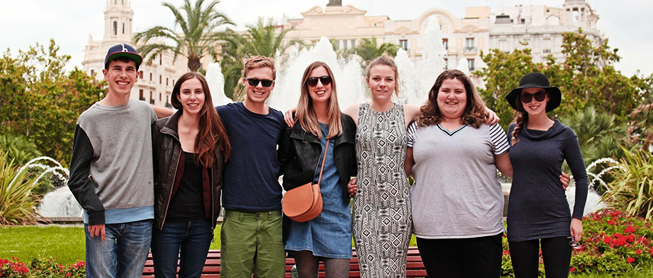 Students posing outside in front of a Spanish fountain and building